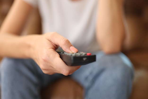 Woman holds remote control in her hand while sitting on sofa