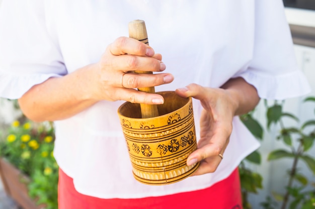 A woman holds a rustic wooden mortar in her hands and kneads peppermint