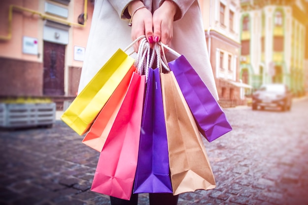 A woman holds shopping bags in front of a city street.