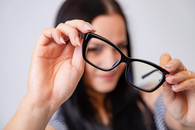 woman holds and shows eyeglasses with black rim on a white background. Close-up