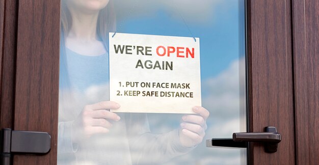 Woman holds sign behind the glass door of store