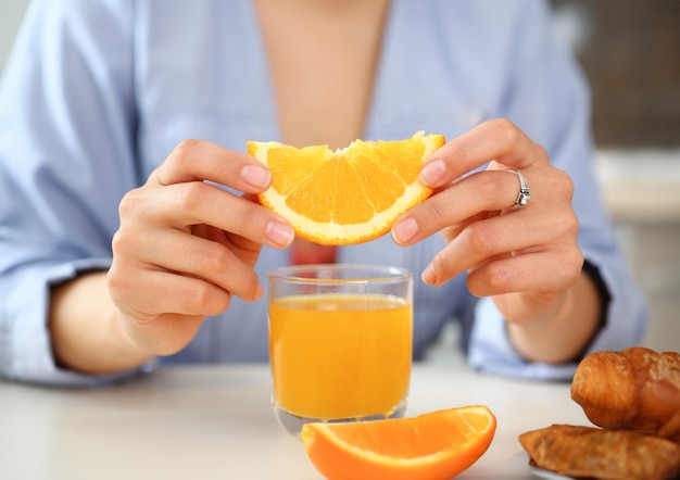 a woman holds a slice of sliced orange in her hand during an early breakfast in the kitchen the concept of a healthy diet