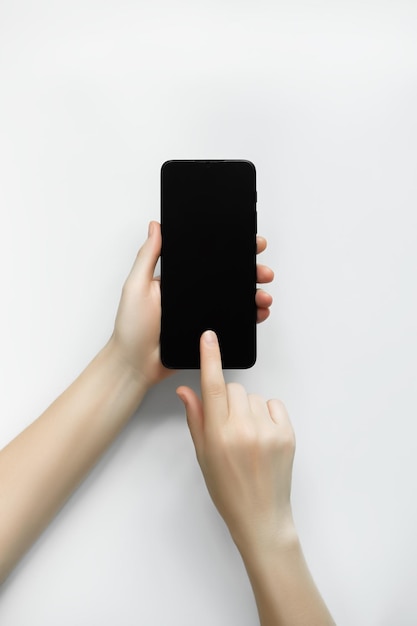 a woman holds a smartphone in her hand and points her finger at a blank black screen top view