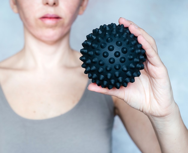 A woman holds a spiky trigger point massage ball used for muscle pain relief