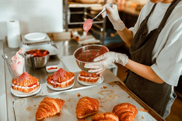 Woman holds spoon with pouring down frosting in craft bakery shop