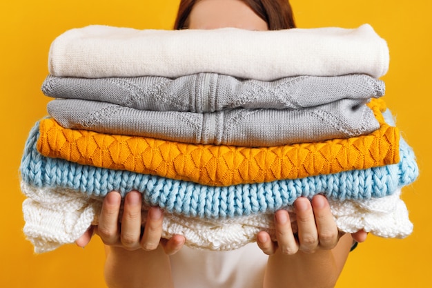 A woman holds a stack of warm knitted clothes