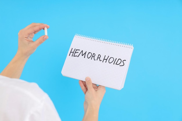 Woman holds text hemorrhoids and suppository on blue background