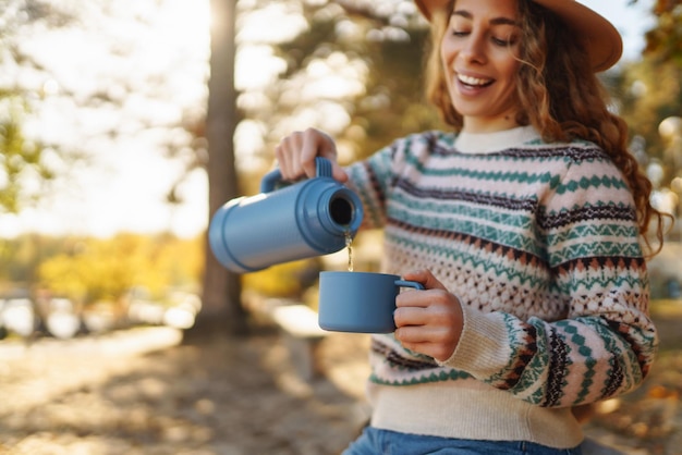 Woman holds thermos and drinks tea in sunny autumn forest vacation travel lifestyle concept