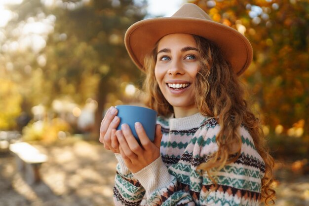 Woman holds thermos and drinks tea in sunny autumn forest Vacation travel lifestyle concept