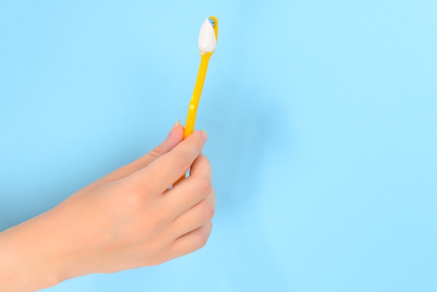 Woman holds toothbrush with toothpaste in her hand on a blue wall.