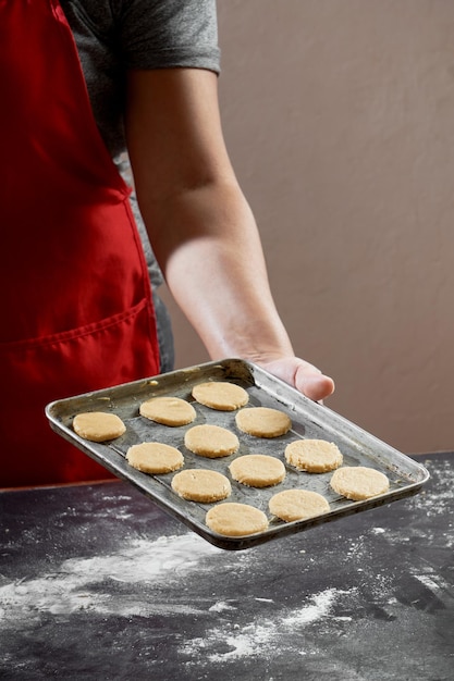 A woman holds a tray of cookies on a table.