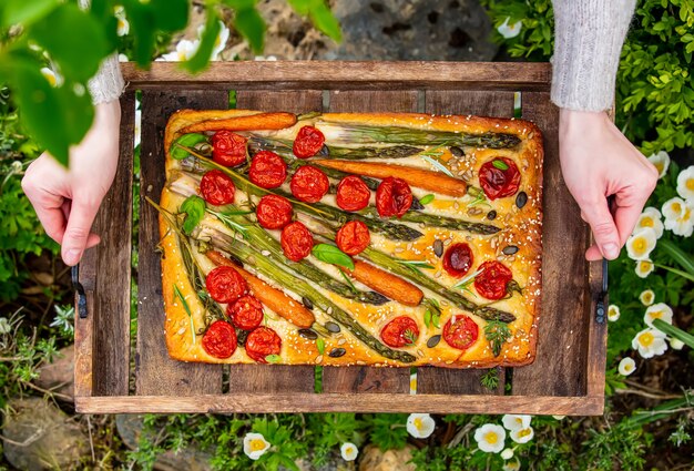 Woman holds a tray of focaccia in the courtyard, with flowers