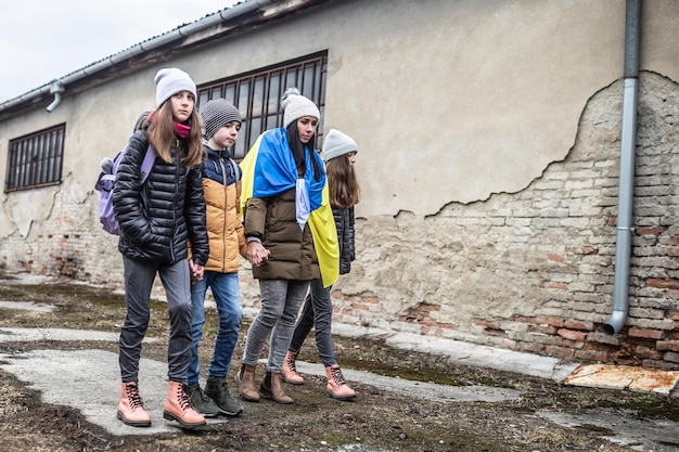 Woman holds Ukrainian flag as she flees the conflict with Russia with three kids in a derelict surroundings