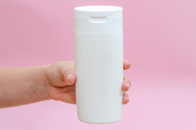 Woman holds a white bottle cream lotion gel shampoo for cosmetic products isolated on pink background