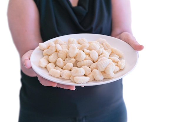 Una donna tiene un piatto bianco con gnocchi isolato su uno sfondo bianco cucina tradizionale pasta per gnocchi gourmet italia gustoso cibo italiano fare il pranzo