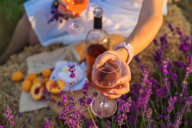 女性はグラスにワインを持っています。ラベンダー畑でのピクニック。セレクティブフォーカス。