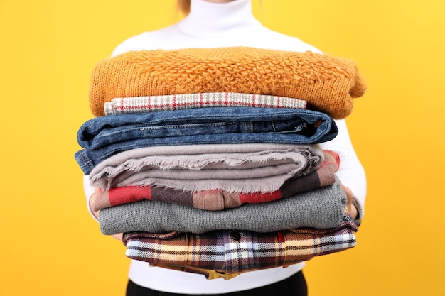 Woman holds winter clothes on yellow background.