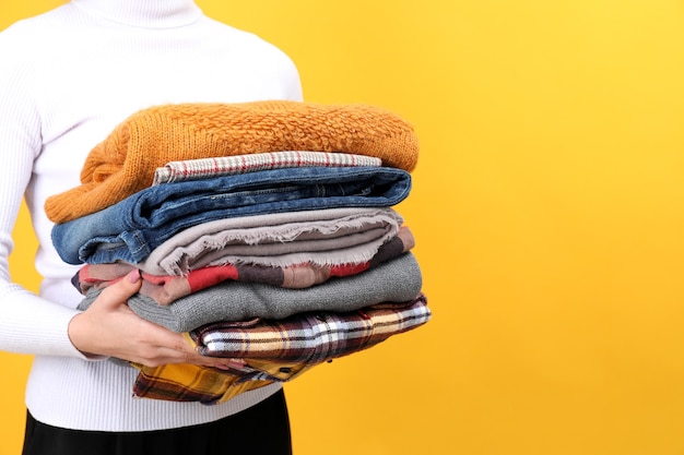 Woman holds winter clothes on yellow background.