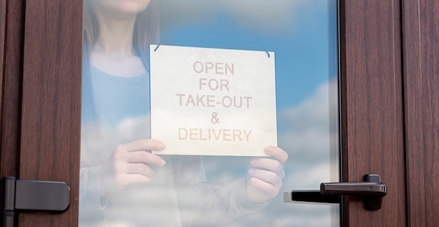 Woman holds the wooden sign with text: Open for take-out and delivery