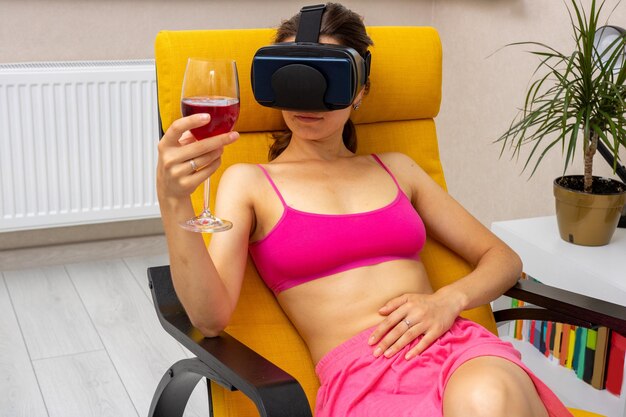 Woman at home in armchair with glass of wine and virtual glasses relaxes