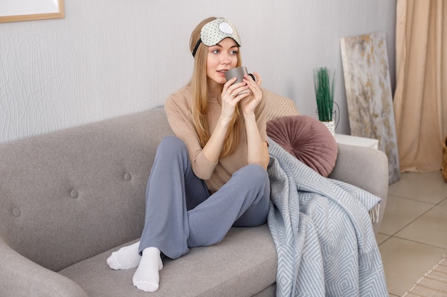 Woman in home clothes with a cup on the sofa at home