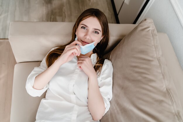 Woman at home on couch wearing mask taking her on and off