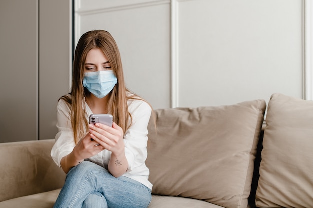 Woman at home on couch wearing mask using phone