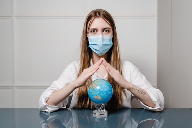 Woman at home behind desk wearing mask and holding planet earth globe