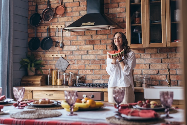 Woman at home eating watermelon in the kitchen.