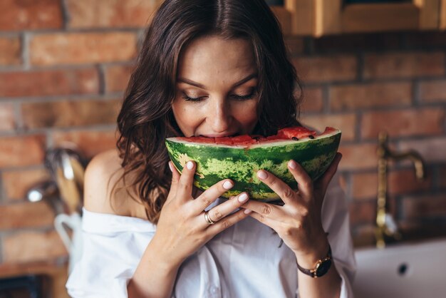 Woman at home eating watermelon in the kitchen.