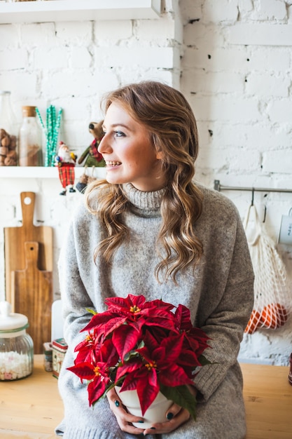 彼女の手でクリスマスの花を持って家にいる女性