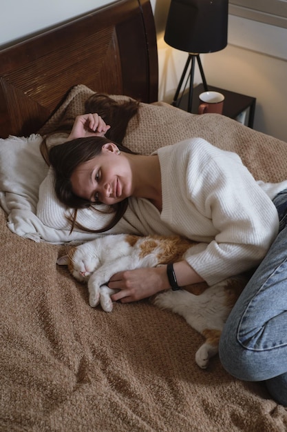 Woman at home holding her cat room interior on the bed