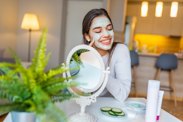 Foto la donna a casa sta applicando la maschera per il viso. procedure cosmetiche, maschera per la cura della pelle, donna giovane. bella donna con maschera facciale.