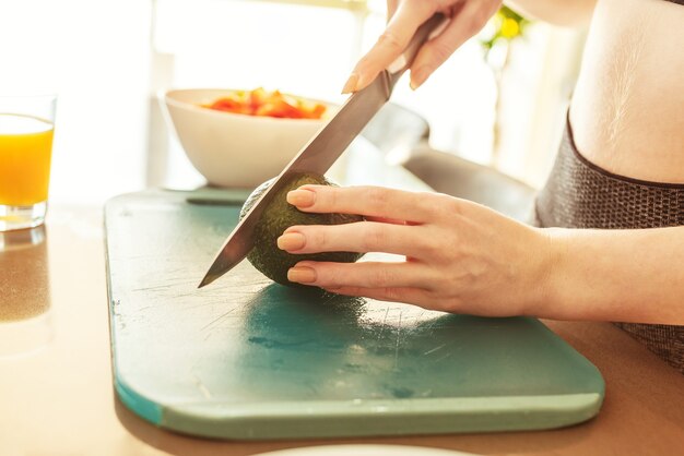 家庭の台所で健康的な食事のためにアボカドを切る女性