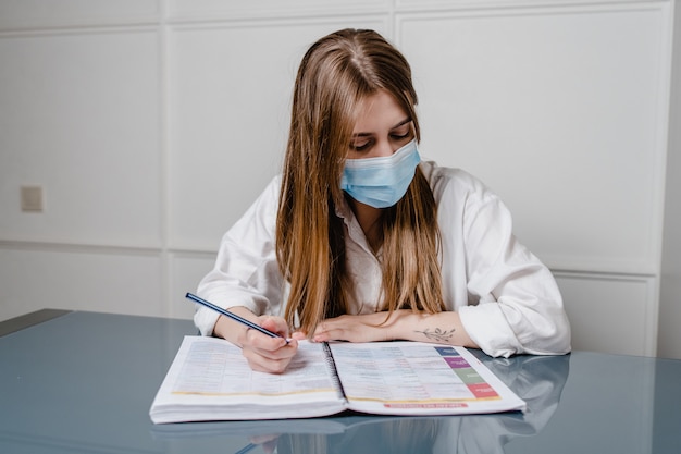 Woman at home office wearing mask and learning with study books