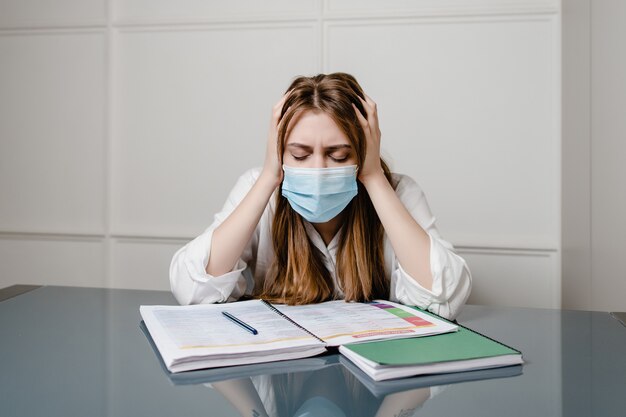 Woman at home office wearing mask and learning with study books