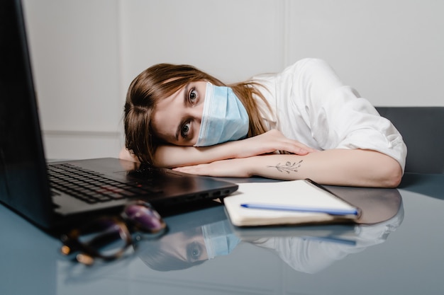 Photo woman at home office with laptop wearing mask and sleeping tired