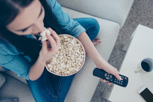 Woman at home on sofa eating popcorn