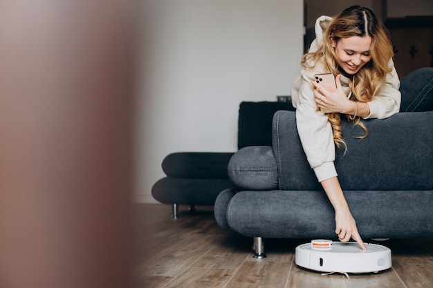 Photo woman at home watching robot vacuum cleaner tiding the house