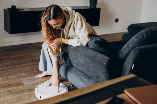 Woman at home watching robot vacuum cleaner tiding the house