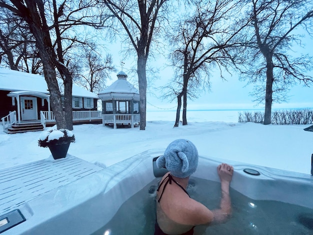 Foto donna in una vasca idromassaggio che guarda un lago coperto di neve