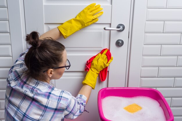 Woman housekeeper wipes the door with rag.