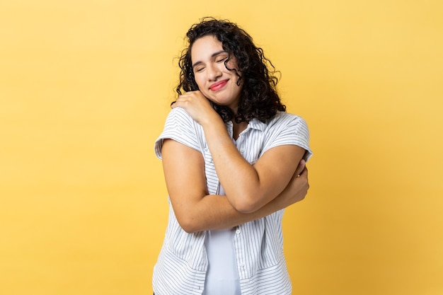 Woman hugging herself and smiling with dreamy satisfied expression love myself gesture