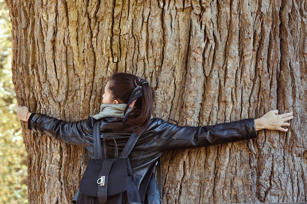 Woman hugging huge tree trunk. Perennial tree.