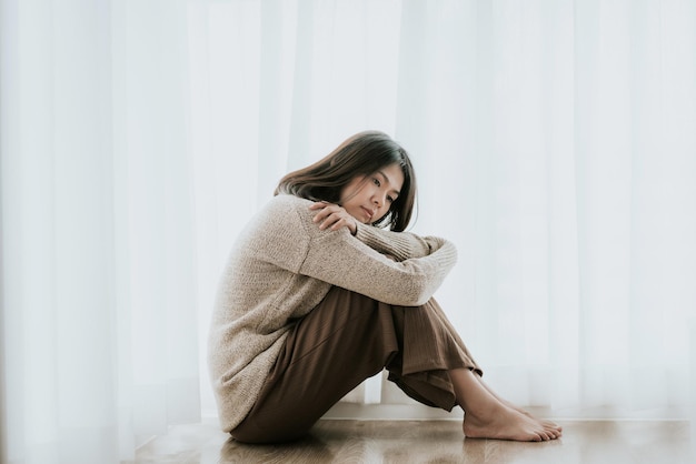 家の床に座っている女性が膝を抱きしめている