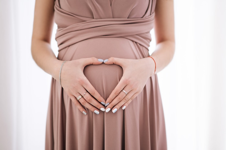 Photo 素敵な妊娠中のおなかを抱き締める女性。ハートの形をした手