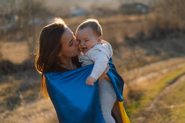 女性は屋外でウクライナの黄色と青の旗に包まれた彼女の幼い息子を抱きしめます