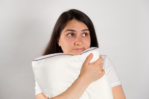 A woman hugs a pillow and looks away on a white background