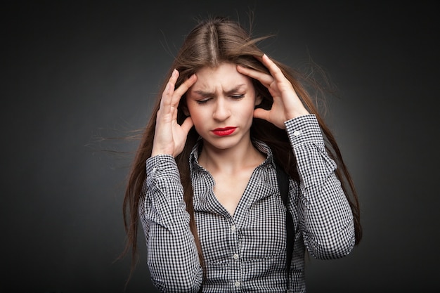 Woman hurts with headache. Studio headshot on black vignette background.