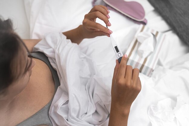 Woman ill and nestled in bed with thermometer tissues nearby contending with fever and sickness